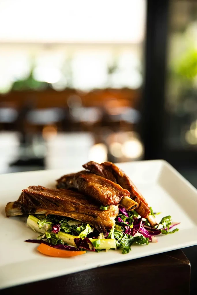 Three glazed ribs, mixed greens, and orange slices on a white plate.