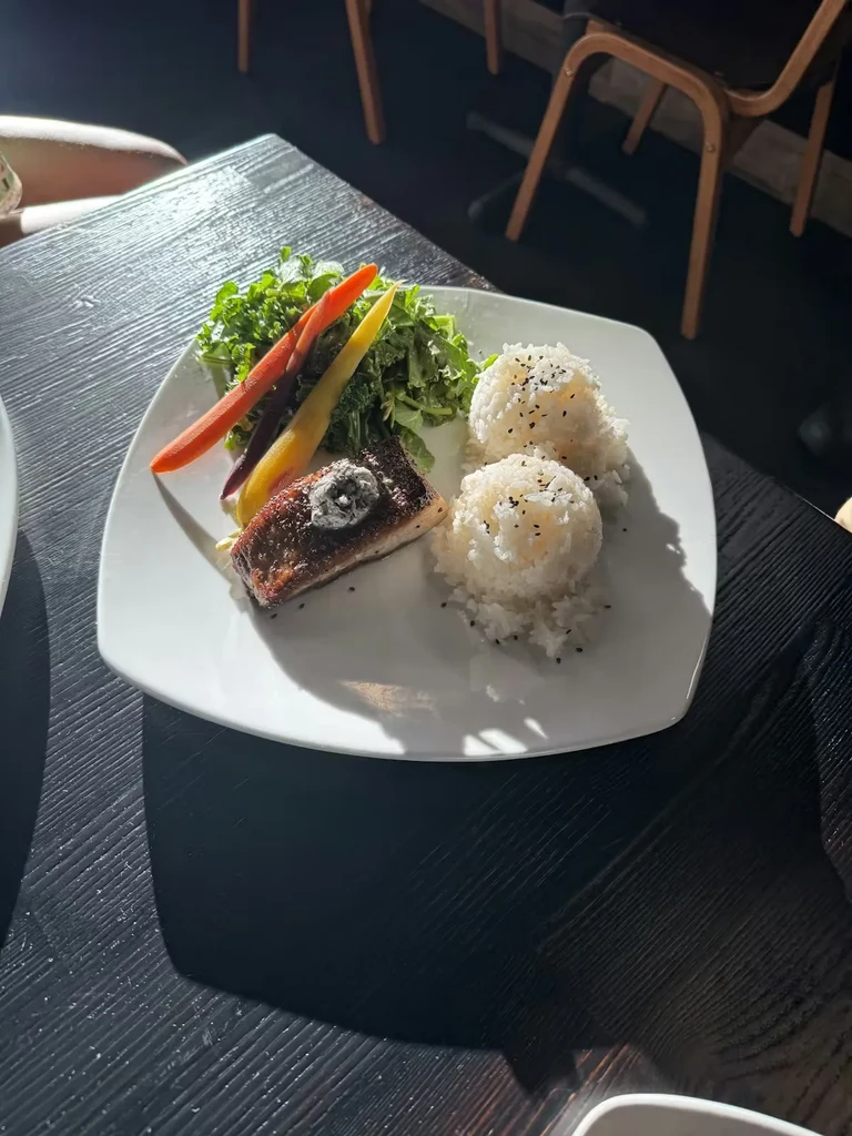 Plate of pan-seared fish, colorful carrots, green salad, and sesame rice.