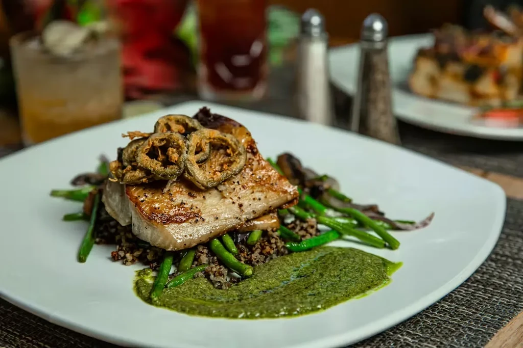 Pan-seared fish, crispy peppers, green beans, grain, and green sauce.