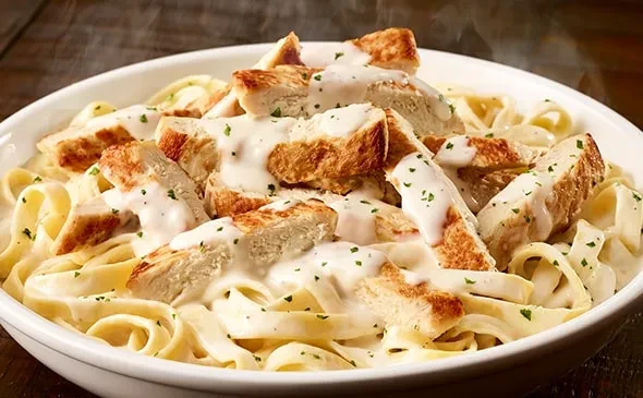 Steaming fettuccine Alfredo with grilled chicken and herbs.