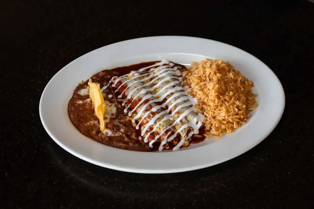 Three enchiladas with red sauce, crema, refried beans, and rice.