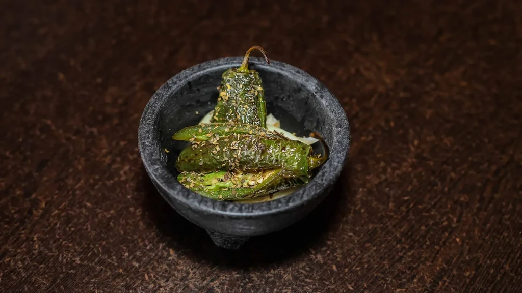 Roasted green peppers with herbs and chili flakes in a stone bowl.