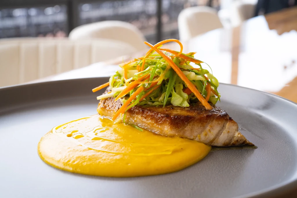 Artfully plated fish on vibrant yellow purée with julienned vegetables.