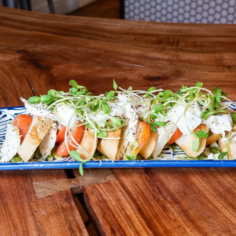 Close-up of bruschetta appetizers with tomato, mozzarella, pesto, and sprouts.