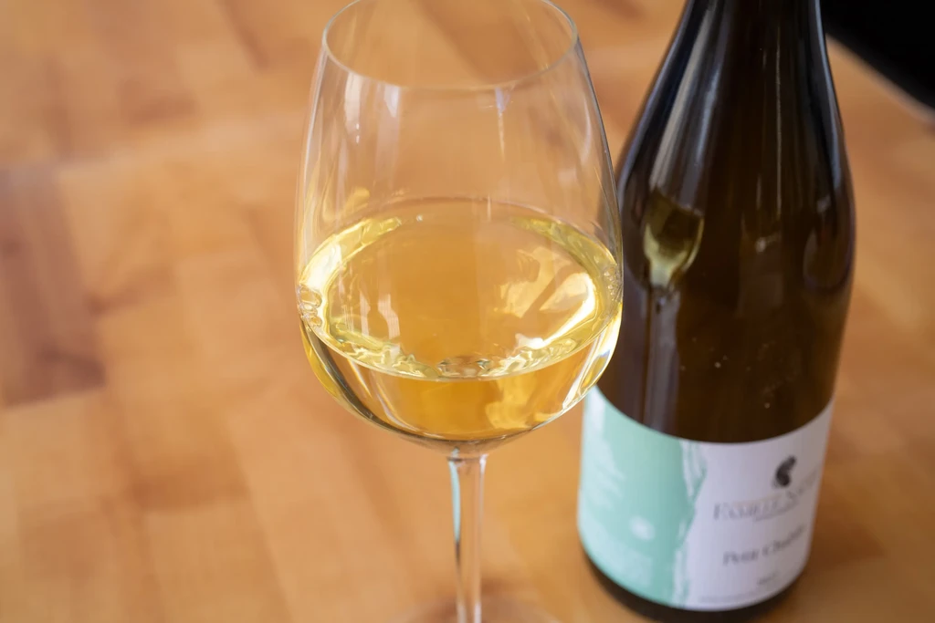 Clear glass of white wine on wood with a dark bottle.