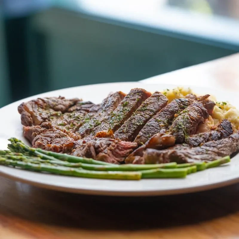 Sliced steak, asparagus, and mashed potatoes on a white plate.