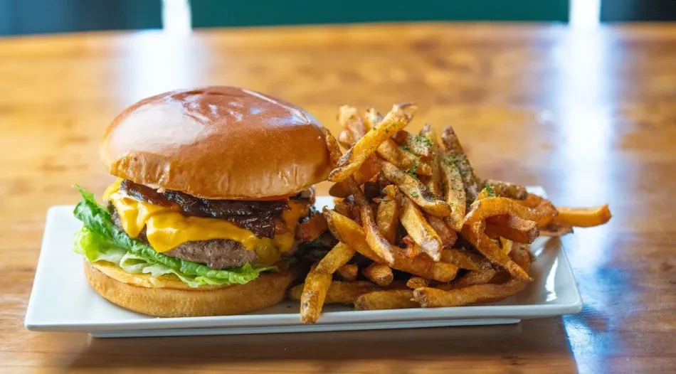 Close-up of a cheeseburger and herb-seasoned fries on a white plate.