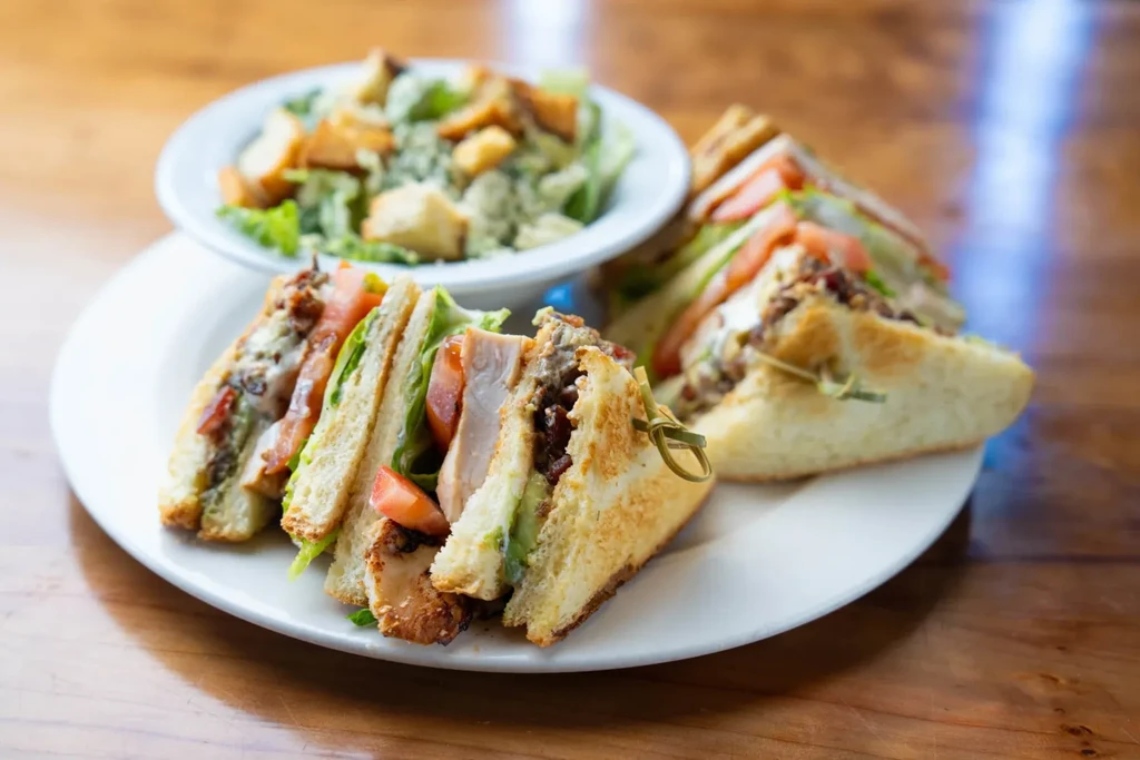 A club sandwich, cut into triangles, served with a Caesar salad.