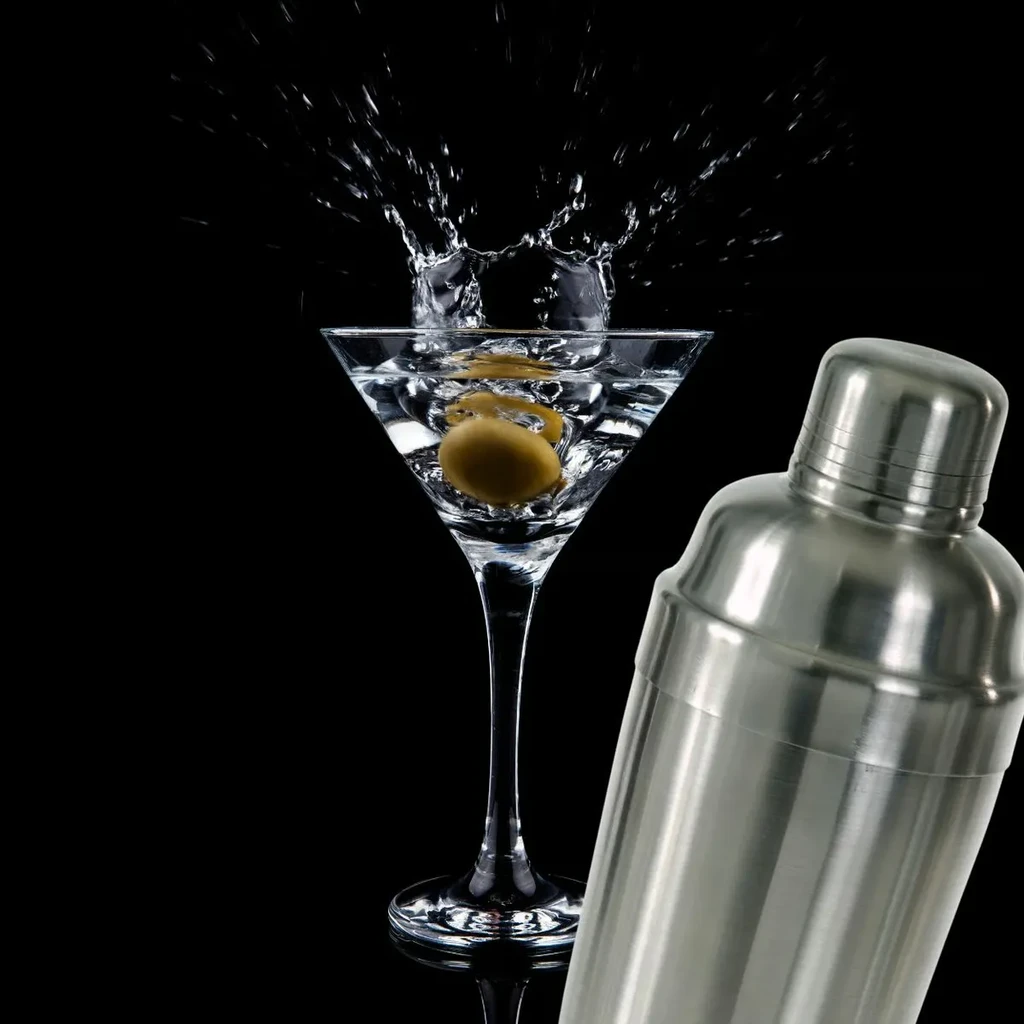 High-speed shot: Martini glass splashing with olives, next to shaker.