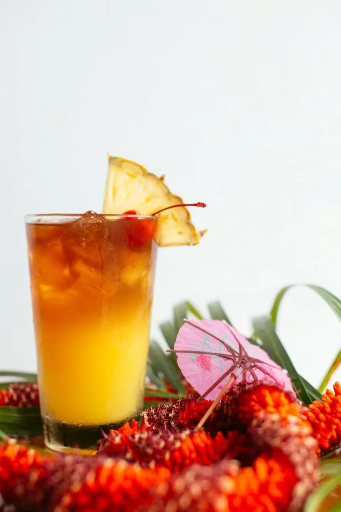 Vibrant layered tropical cocktail with pineapple and cherry garnish.