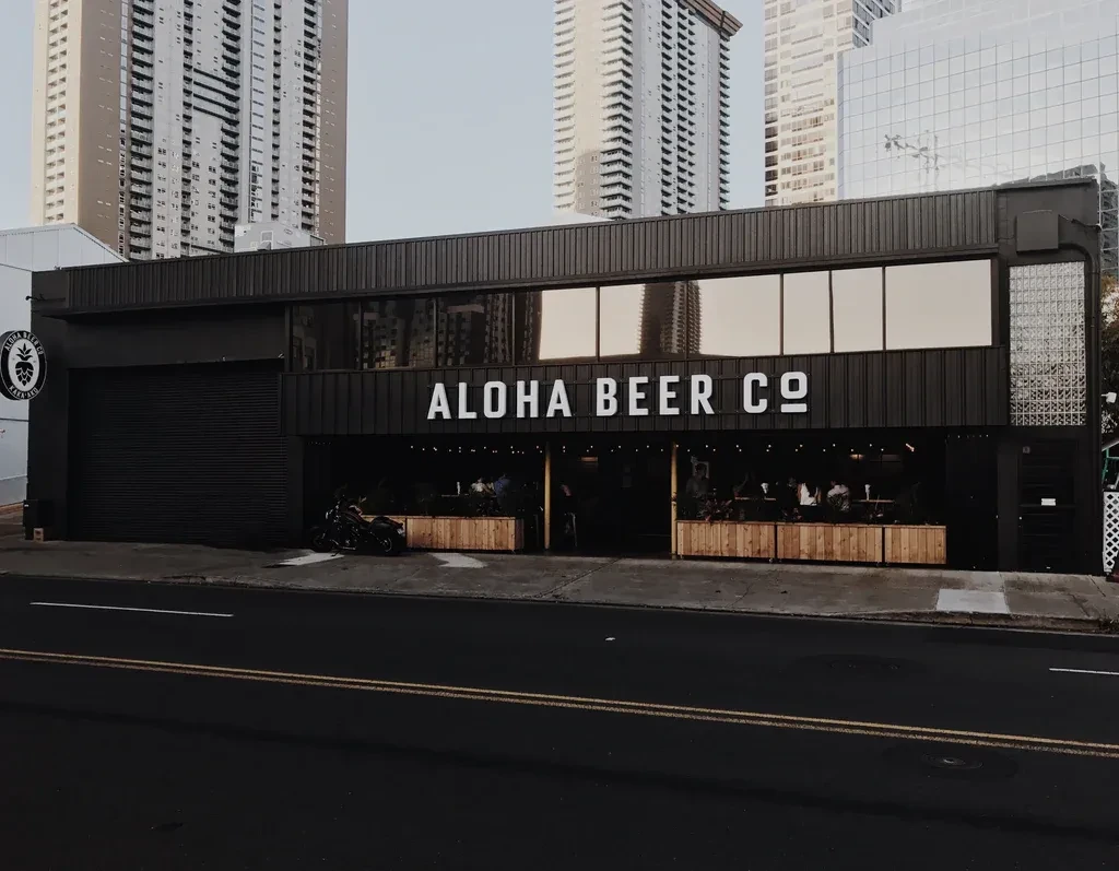 Aloha Beer Co's modern dark building, open-air with people socializing.