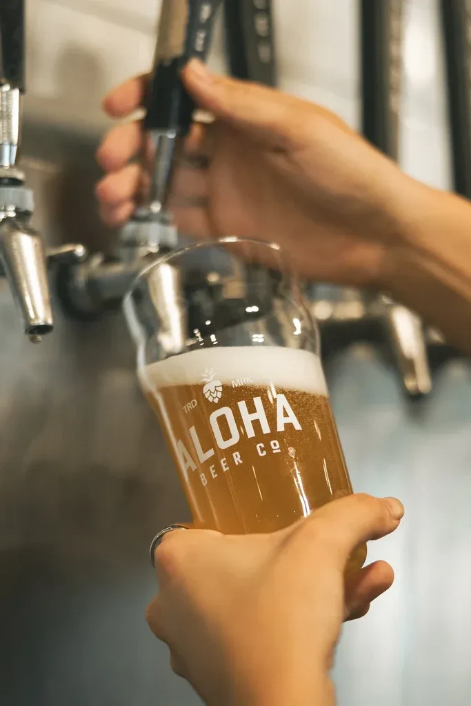 Hands pouring amber beer into a logo glass from a silver tap.
