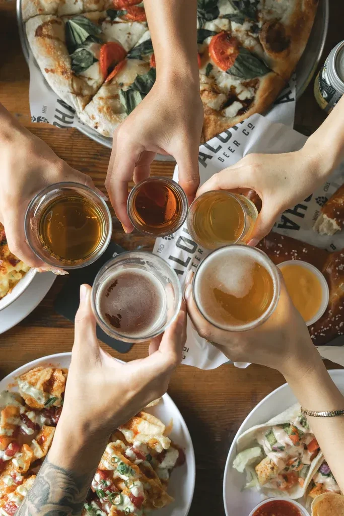 Hands toasting drinks above a food spread at Aloha Beer Co.