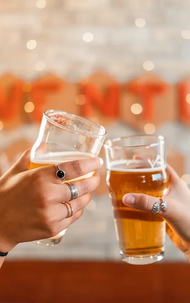 Close-up of two hands toasting with different beers.