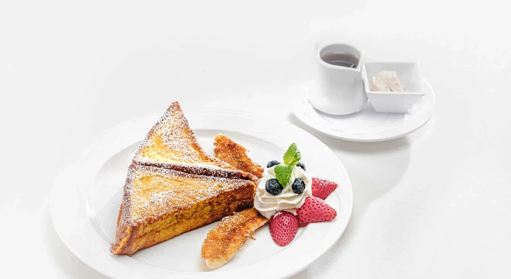 Plated French toast with powdered sugar, whipped cream, berries, caramelized bananas.