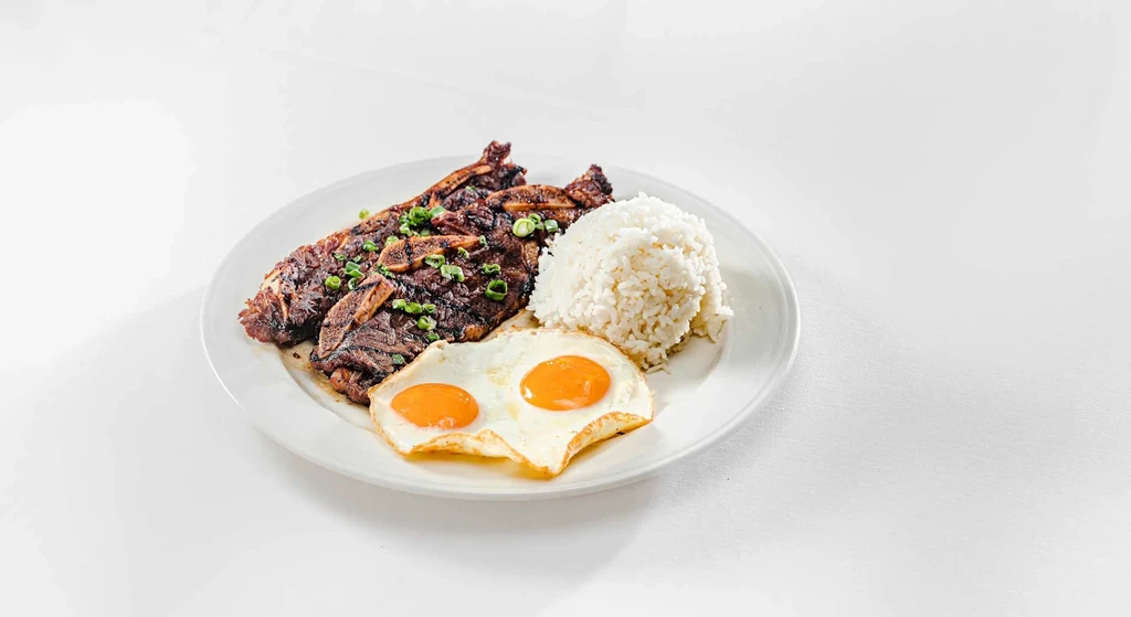 Grilled short ribs, white rice, and two fried eggs on an oval plate.