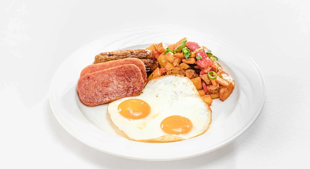 Plate with fried eggs, Spam, sausage, and seasoned home fries.