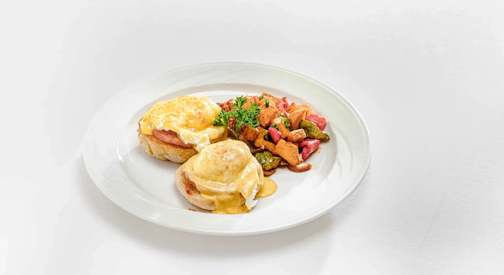 Two Eggs Benedict with roasted potatoes and vegetables on a white plate.