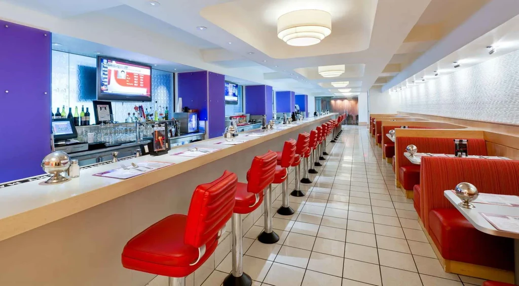 Modern diner interior with red stools, purple wall, and red booths.