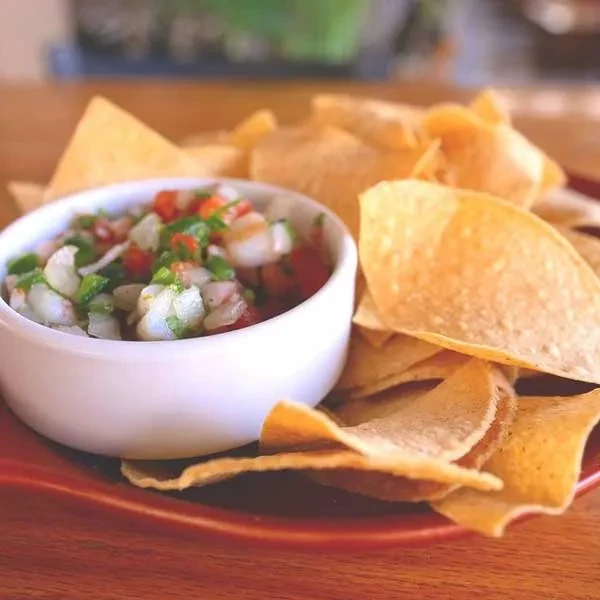 White bowl of shrimp ceviche and tortilla chips on a brown plate.