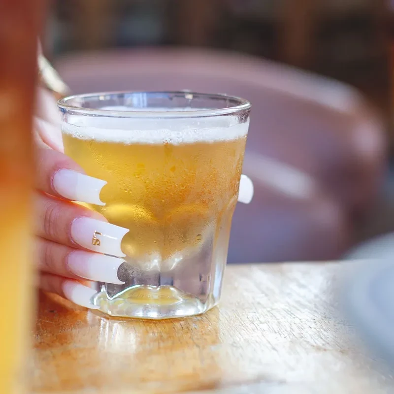 Hand with 'LS' ombre nails holds a frosty golden beer.