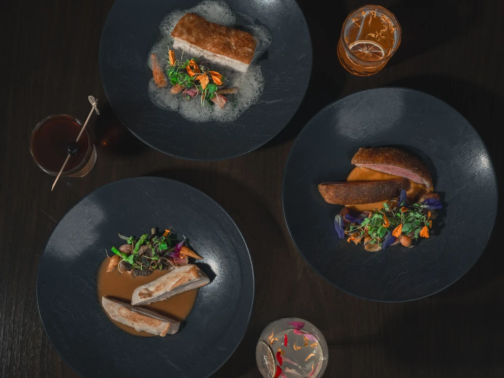 Overhead of three artfully plated gourmet dishes and drinks.