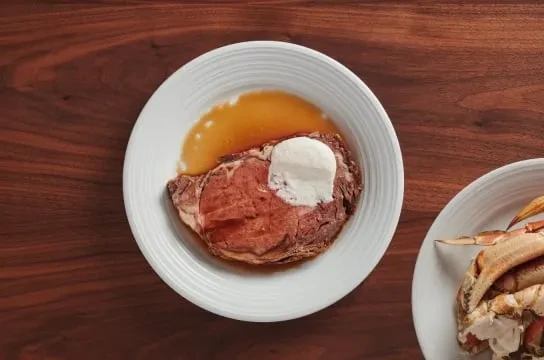 Medium-rare roast beef with cream sauce, crab legs, on wood table.