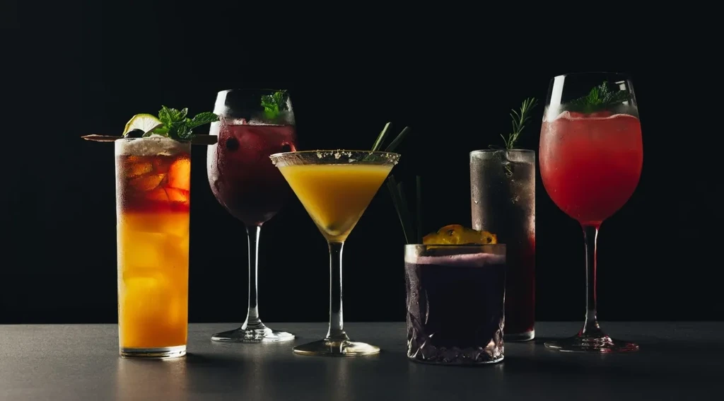 Six distinct, colorful cocktails professionally arranged against a dark background.