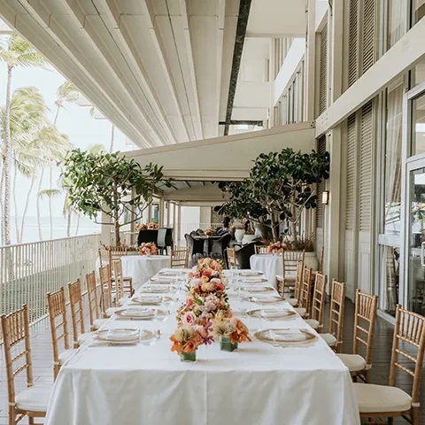 Elegant dining table with gold chairs set on a tropical balcony.