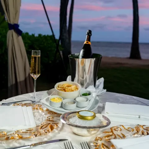 Elegant outdoor table with champagne, caviar, appetizers, and ocean view at dusk.