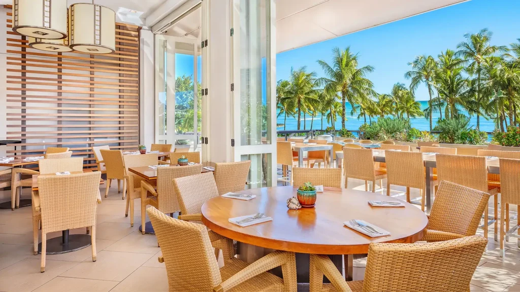 Empty tropical restaurant with rattan tables overlooking a turquoise ocean.