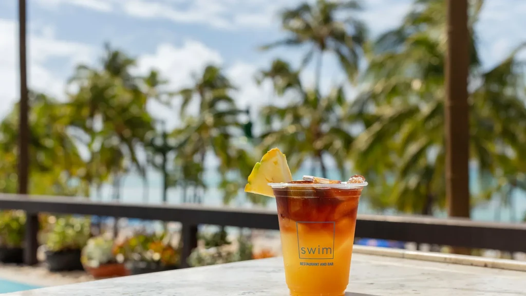 Layered drink with pineapple garnish at an outdoor tropical bar.