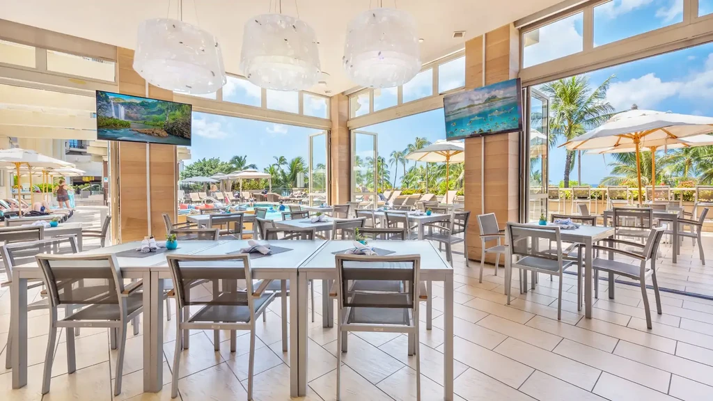 Bright, empty indoor-outdoor dining area overlooking a tropical pool and ocean.