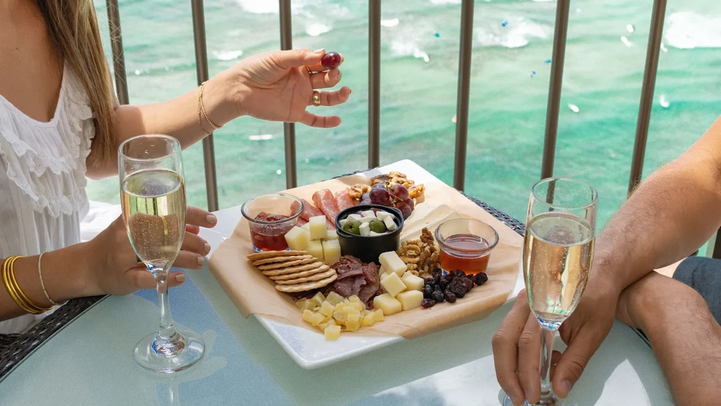 Gourmet charcuterie board with champagne flutes and ocean view.