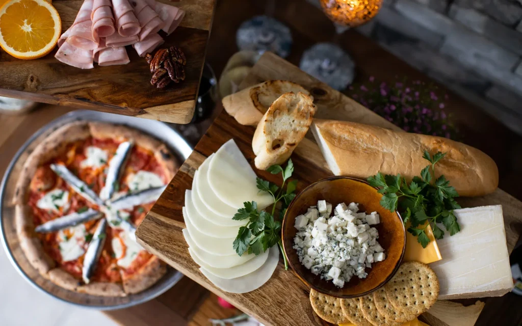 Rustic food spread with cheeses, meats, baguette, and sardine pizza.