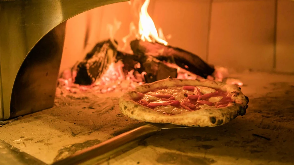 Partially cooked pizza with cheese and peppers inside a flaming wood oven.