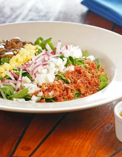 Colorful salad with bacon, radishes, egg, mushrooms in a white bowl.