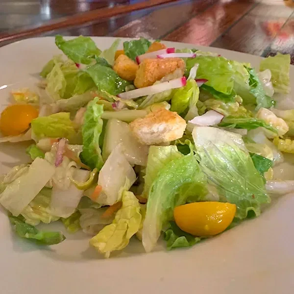 Close-up of a vibrant salad with lettuce, croutons, radishes, yellow tomatoes.