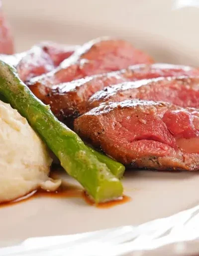 Sliced medium-rare meat, green asparagus, mashed potatoes, and sauce on a plate.