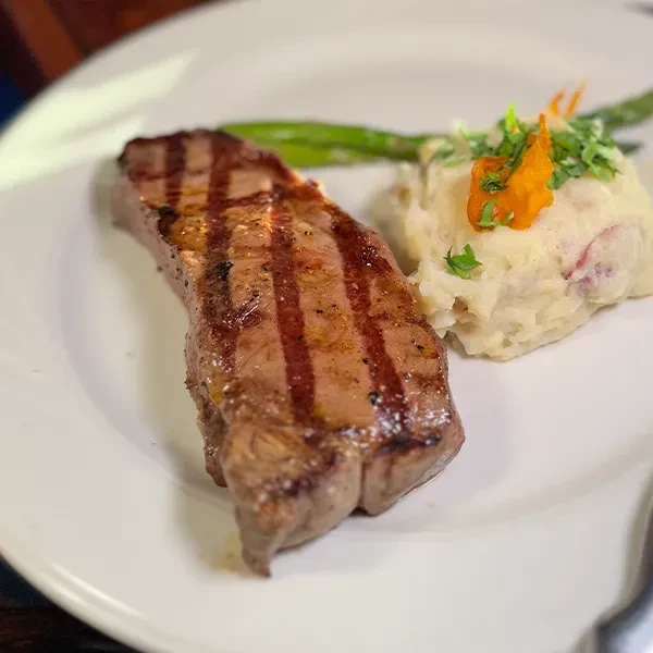 Grilled steak with rustic mashed potatoes and asparagus on a white plate.