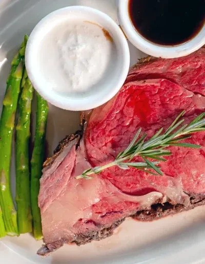 Plated rare prime rib with rosemary, asparagus, and two sauces.
