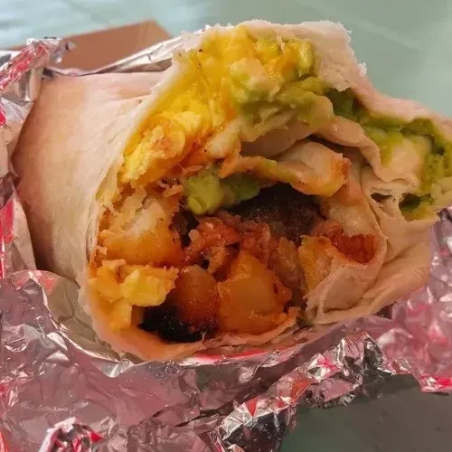 Sliced breakfast burrito unwrapped, revealing eggs, avocado, and hash browns.