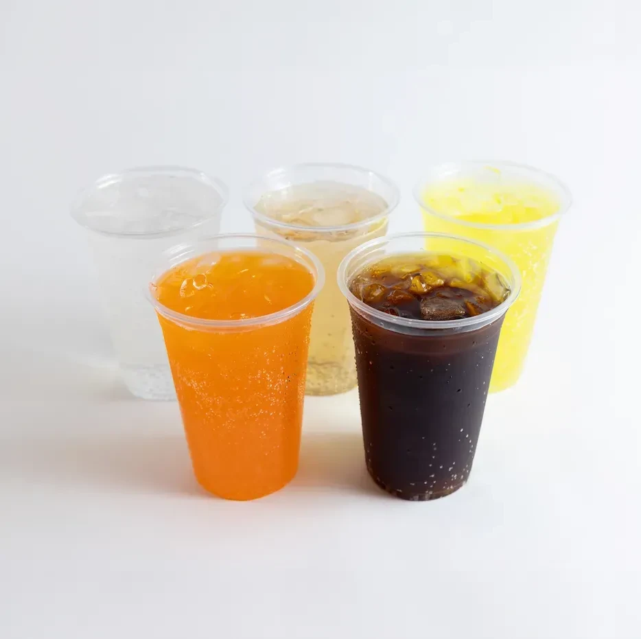 Five transparent plastic cups of various colorful iced drinks with condensation.