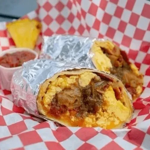 Two burritos, one open with eggs, meat, salsa, and a pastry.