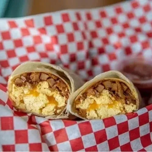 Breakfast burrito halves with eggs, cheese, and sausage on checkered paper.