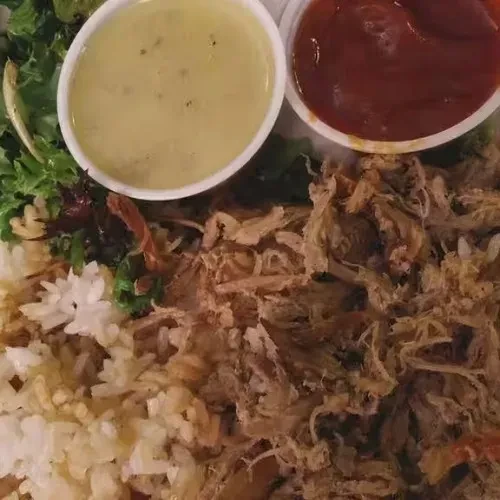 Plate with shredded meat, mixed rice, greens, and two sauces.