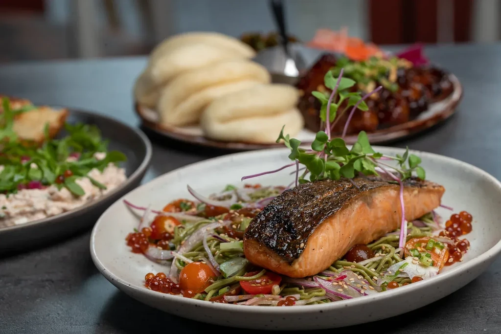 Professionally styled shot of crispy salmon on noodles with various side dishes.