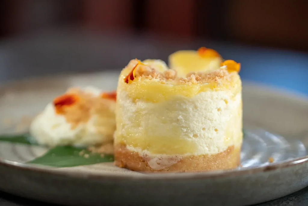Layered dessert with yellow top, white cream, orange, and green leaf.