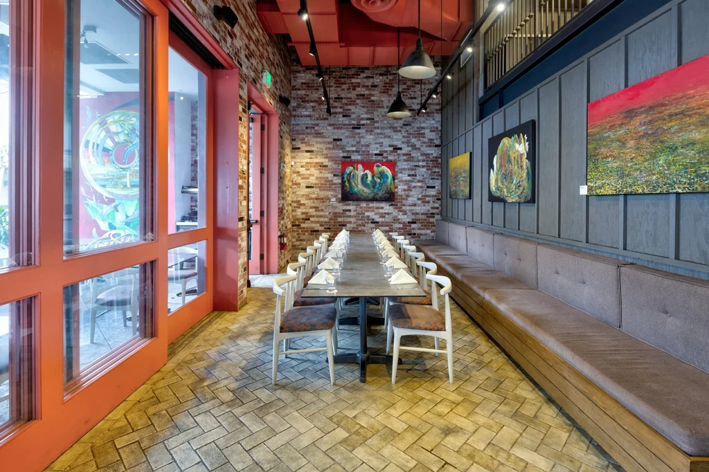 Modern restaurant interior with long table, banquette, art, and brick wall.