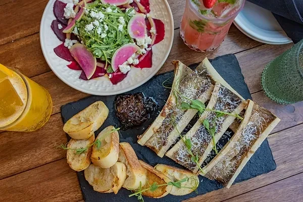 Overhead view of salad, bone marrow, and drinks on rustic wood.